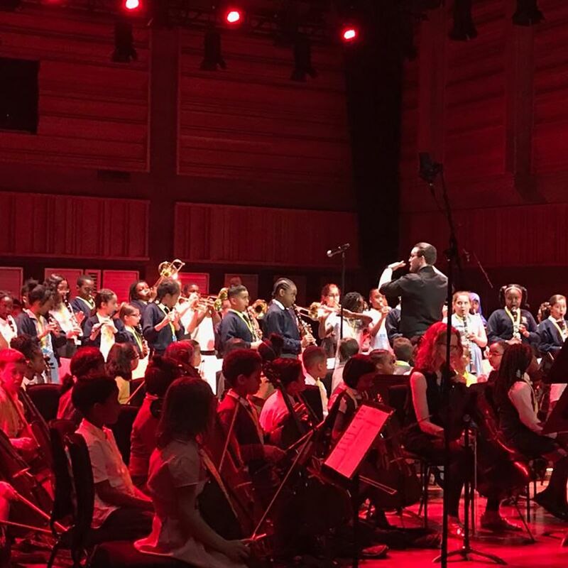 A children's orchestra performing on stage with a conductor standing in the middle