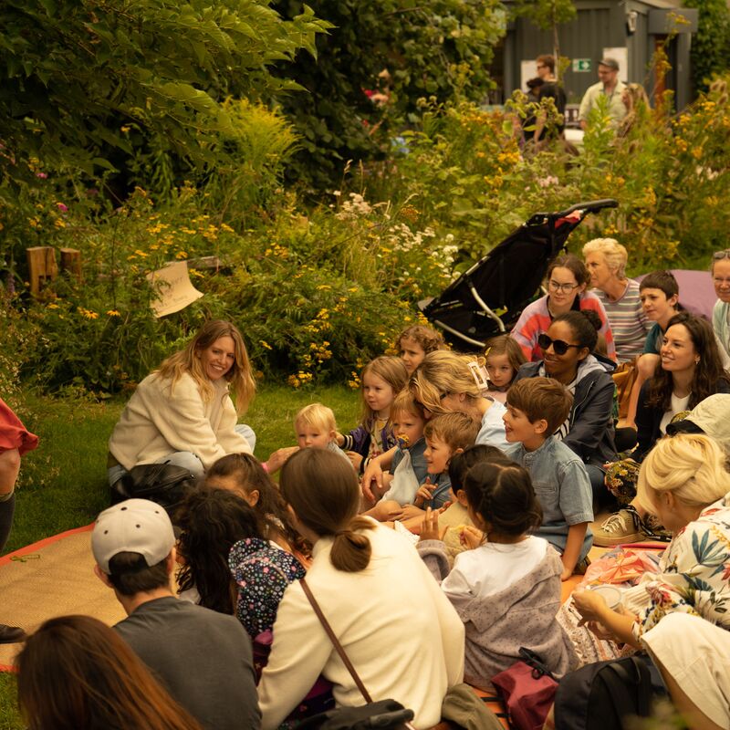 A group of children sat listening to performers in the Queen Elizabeth Roof Garden