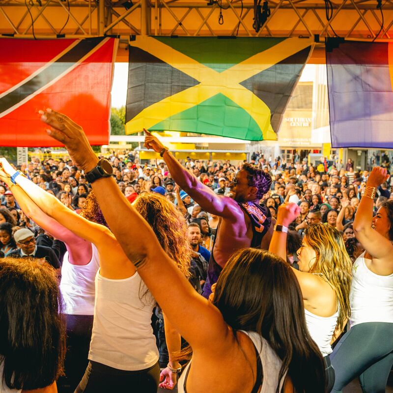 People dance on a stage in the sunshine looking out into a busy crowd.