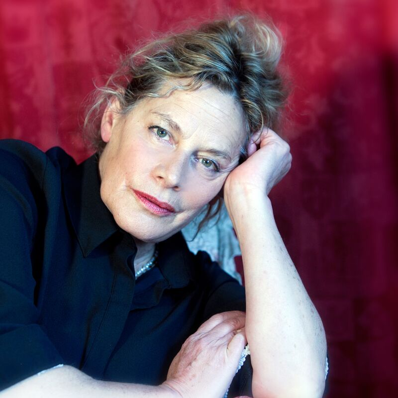 Deborah Levy sits in front of a red curtain and rests her head on her hand.