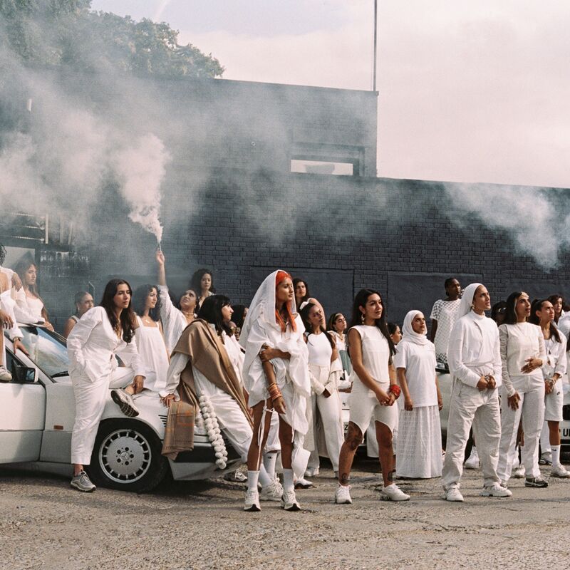 People dressed in white standing next to each other in front of a white car