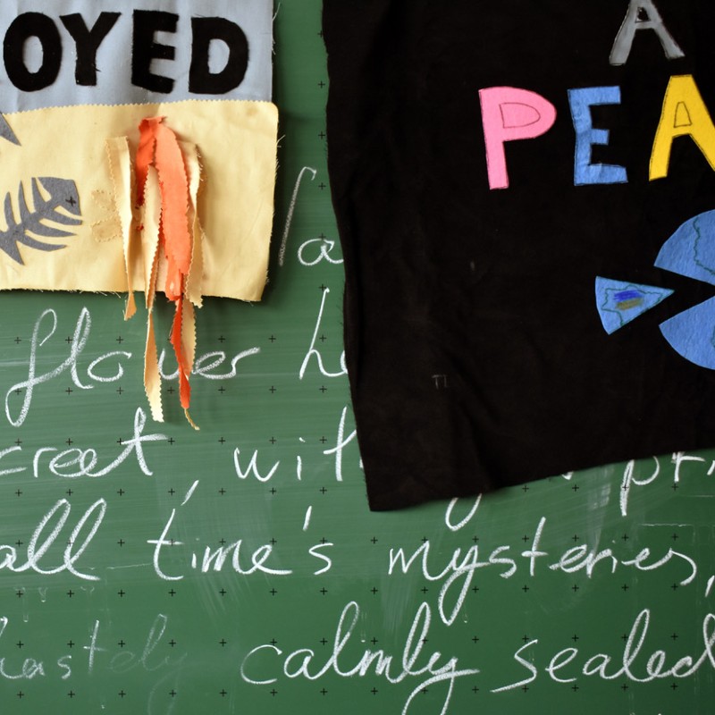 Blackboard covered in writing in white chalk with fragments of paper and material partially obscuring the words.