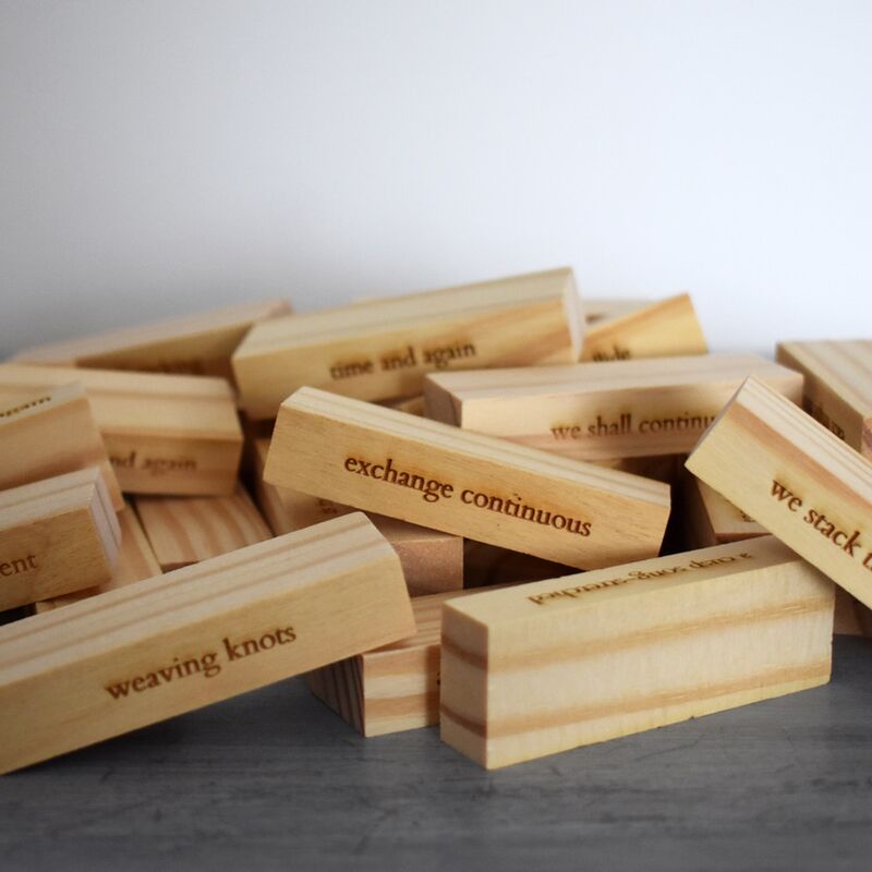 A pile of Jenga bricks scattered on the ground, with lines of poetry carved into the wood.