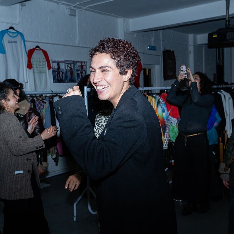 A woman laughing lit by the flash in front of racks of clothing.