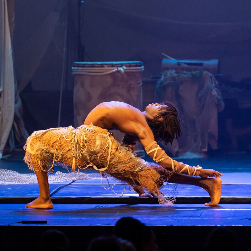 A contortionist in Afrique en Cirque costume in a deep lunge onstage