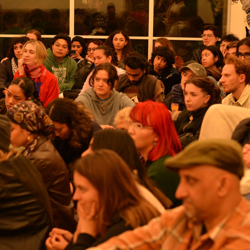 An audience sitting on the floor looking at something on stage off camera.