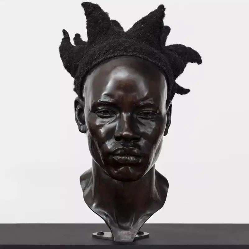 A black head bust of a sculpture featured in Tavares Strachan's exhibition, with a hard to read facial expression and hair pointing upwards..