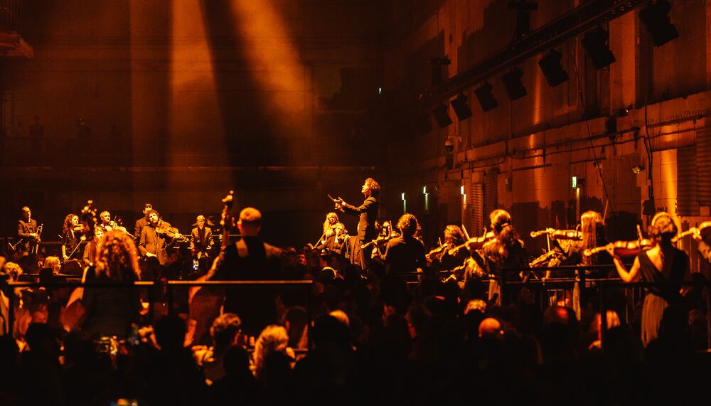 A large orchestra performing in a dark space filled with organge hues