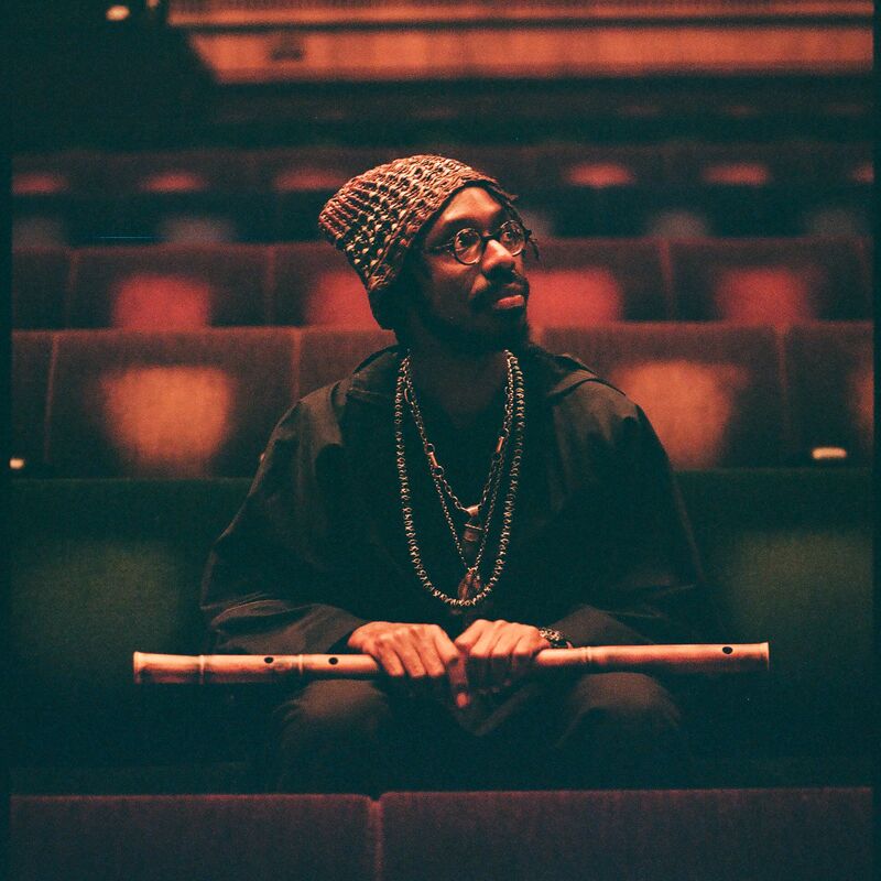 Artist shabaka sits in an empty auditorium holding a wooden flute in his hands