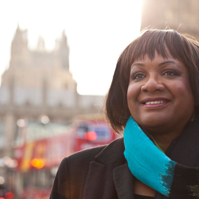 Woman in a black coat and blue scarf looks into the distance.