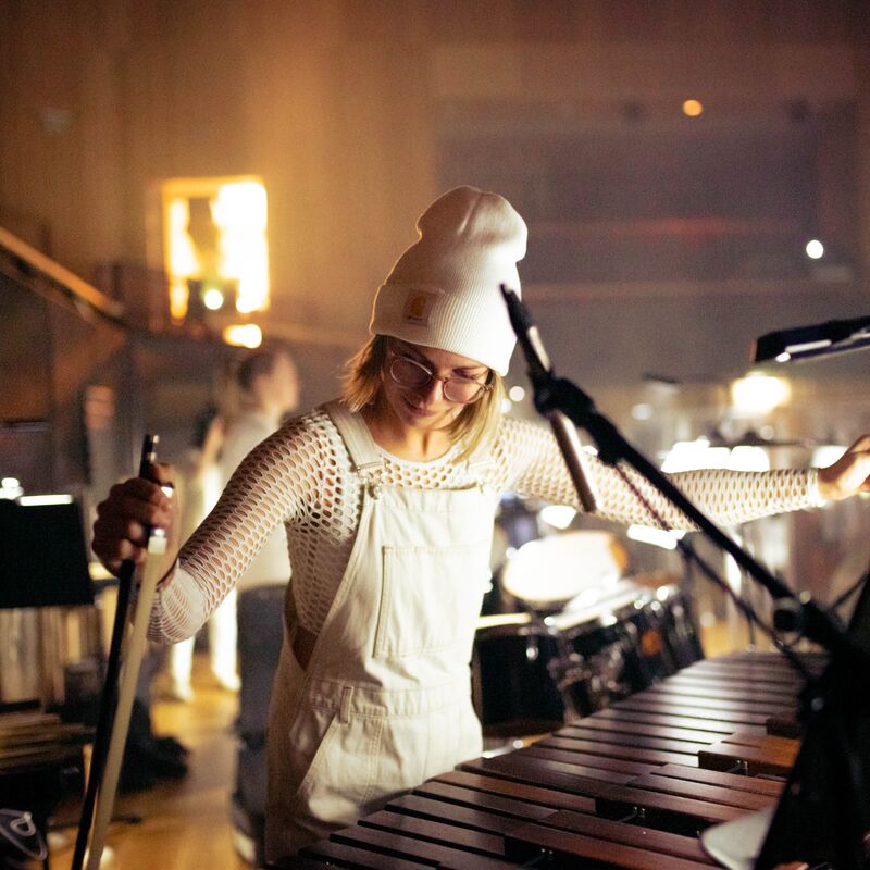 A woman in white dungarees playing percussion