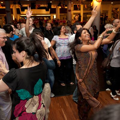 A large group of people dancing together, smiling and lifting their arms up