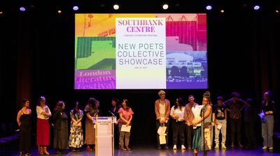 A group of people standing on stage, one holding flowers and speaking into a micropone
