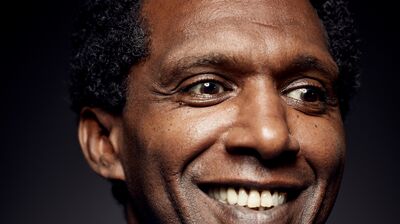Lemn Sissay smiling and wearing a blue jumper against a black background.