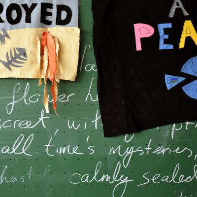 Blackboard covered in writing in white chalk with fragments of paper and material partially obscuring the words.