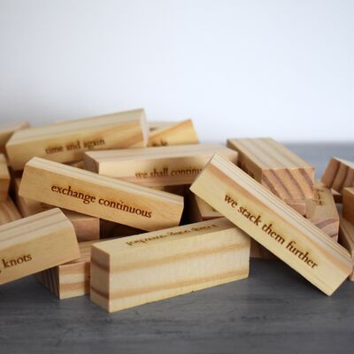 A pile of Jenga bricks scattered on the ground, with lines of poetry carved into the wood.