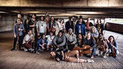 Large group of musicians holding their instruments gather for a photo in a multi-story concrete parking garage