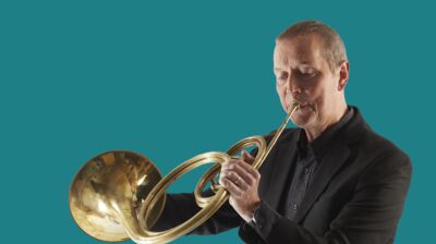 An 18th Century horn being played by Roger Montgomery, a white man dressed in black clothes