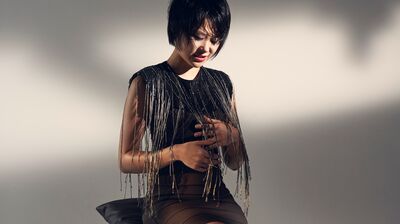 Yuja Wang sitting on a stool with dangles on her dress