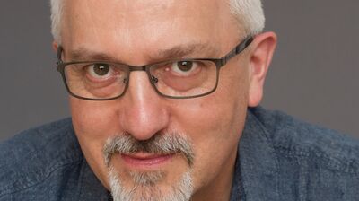 Writer Alan Hollinghurst wears rectangular glasses and looks into the camera