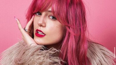 Writer Florence Given wears a fur coat in front of a pink background that matches her hair.