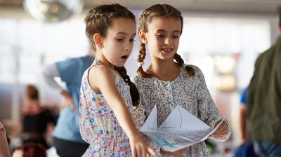 Two girls in floral dresses examining a piece of paper.
