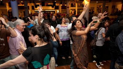 A large group of people dancing together, smiling and lifting their arms up