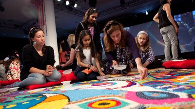 A group participating in a Rangoli Workshop using colourful sand to create patterns on the floor