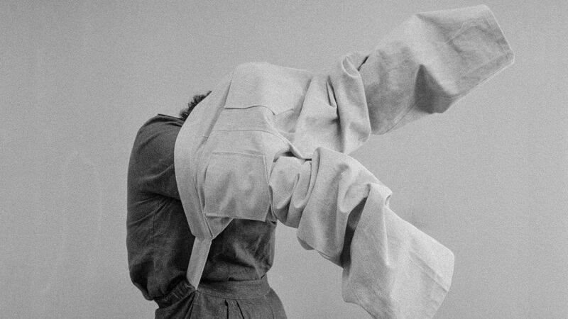 Black and white image of a person trying on suit trousers over their head