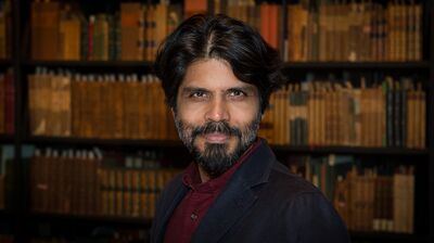 A man in a blazer standing in front of a book case