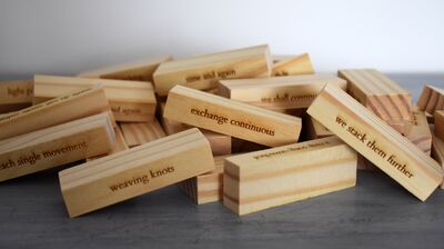 A pile of Jenga bricks scattered on the ground, with lines of poetry carved into the wood.