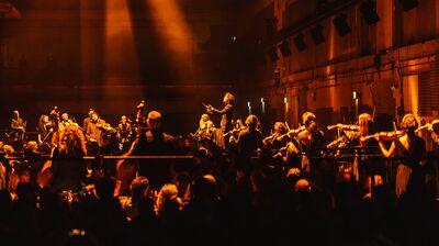 A large orchestra performing in a dark space filled with warm orange hues