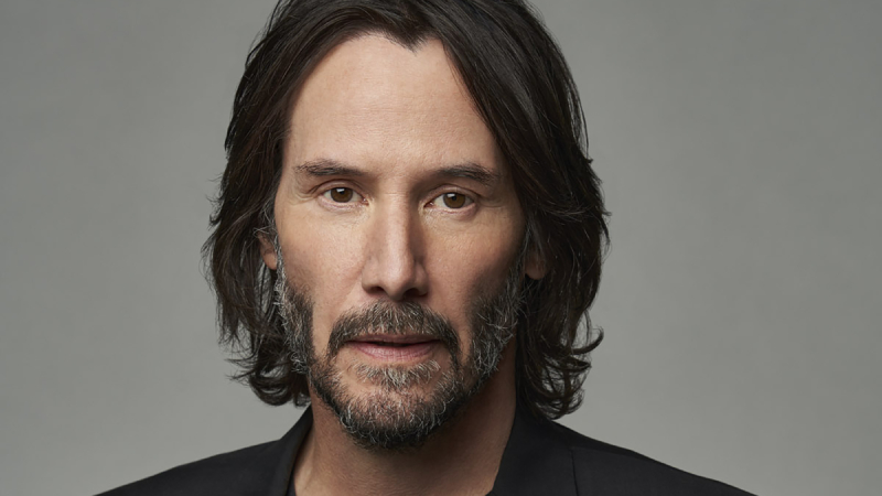 Keanu Reeves wearing black against a grey background.