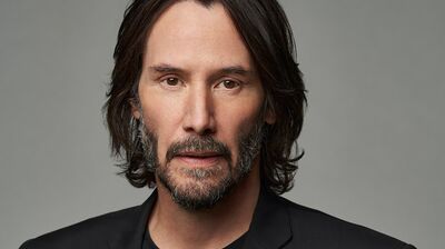 Keanu Reeves wearing black against a grey background.