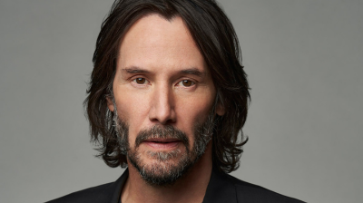 Keanu Reeves wearing black against a grey background.