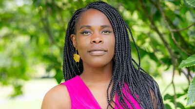 Writer Vanessa Kisuule stands underneath a tree wearing a pink waistcoat.