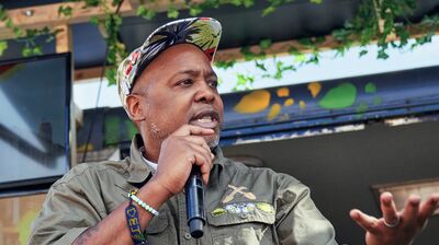 Man wearing green shirt and floral backwards cap using a microphone.