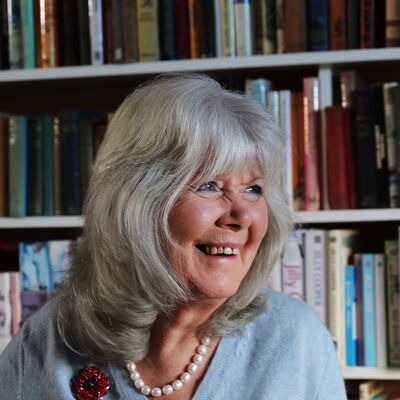 Author Dame Jilly Cooper smiles off camera in front a bookshelf.