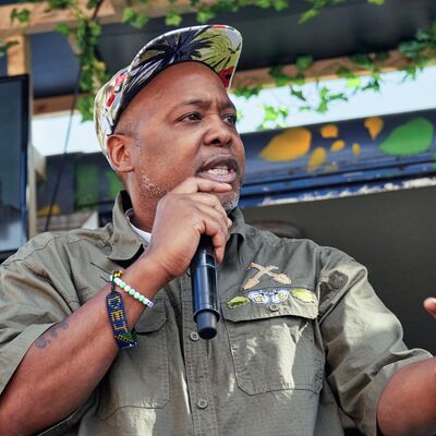 Man wearing green shirt and floral backwards cap using a microphone.