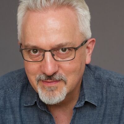 Writer Alan Hollinghurst wears rectangular glasses and looks into the camera