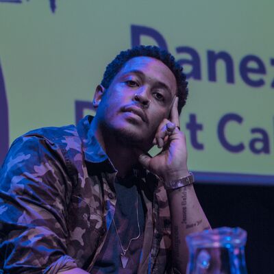 Danez Smith sits onstage, wearing a camo jacket.