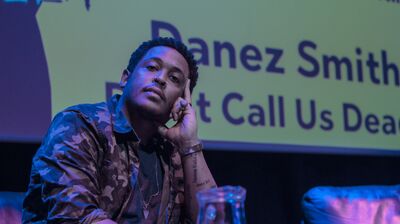 Danez Smith sits onstage, wearing a camo jacket.