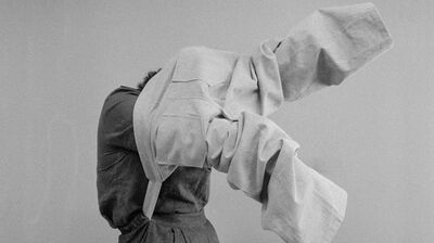 Black and white image of a person trying on suit trousers over their head