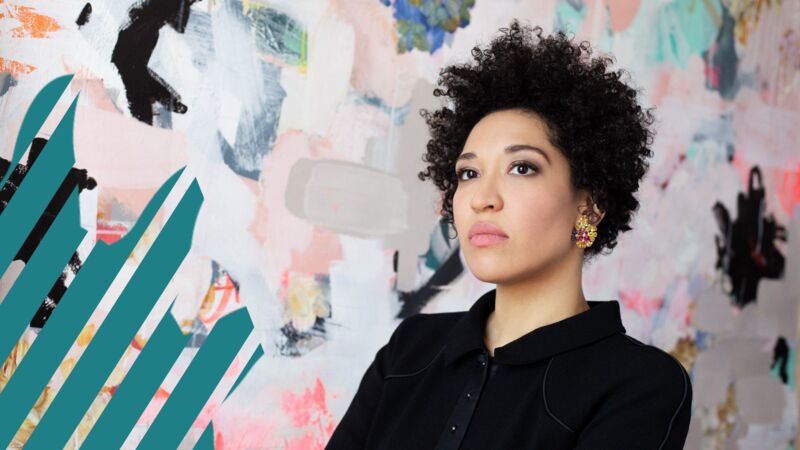 A photograph of Julia Bullock, a woman of mixed heritage in her 30s dressed in a black shirt, standing against a multi-coloured background