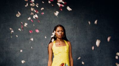 A woman wearing a yellow dress with floral skirt and gold hoop earrings surrounded by falling petals