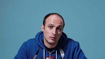 Robert Popper sits at a table with a knife and fork against a blue background