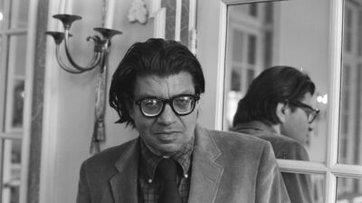 Composer Morton Feldman in black and white standing next to a mirrored door