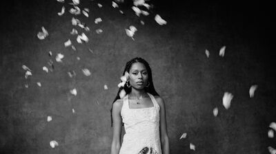 A woman wearing a yellow dress with floral skirt and gold hoop earrings surrounded by falling petals