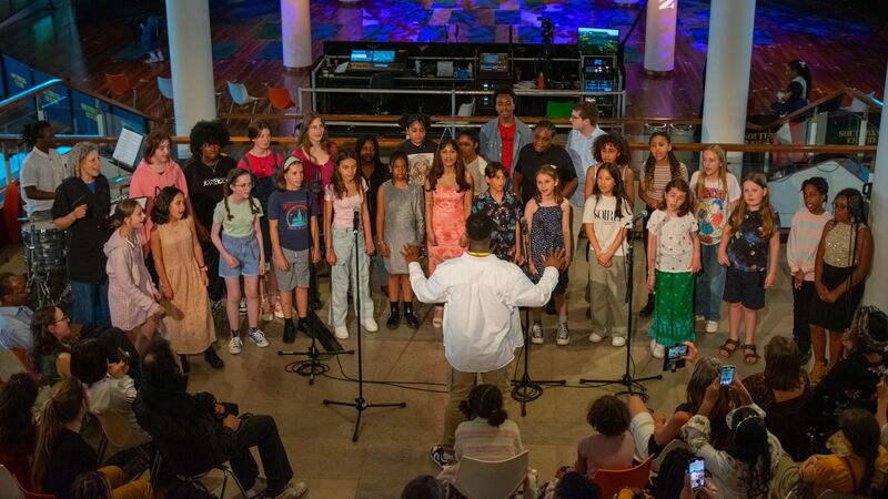 A group of children singing in a choir in front of the Clore Ballroom