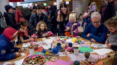 A group of children and parents doing arts and crafts around a wooden table